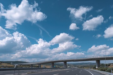 Expansive asphalt highway beneath a vibrant blue sky with soft white clouds and a prominent bridge in the distance creating an inviting scenic route for travel