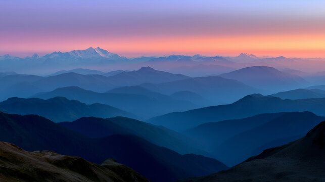 Layered mountain ranges fading into the distance, the foreground in deep shadow and the background glowing in pink and orange dawn hues.