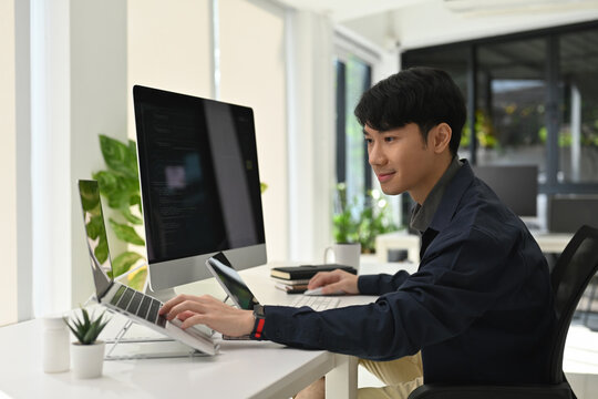 Bright and organized workspace with a focused young coder using multiple devices, ideal concept for modern digital work and remote development