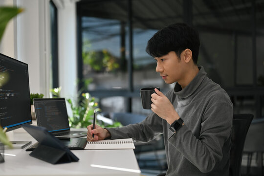 A Software engineer holds a cup and works in a relaxed tech workspace surrounded by greenery and code - Powered by Adobe