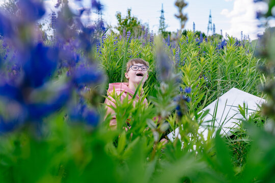 Smiling child with Down syndrome among lupine flowers outdoors