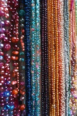 Close-up view of colorful hanging beads in various shapes and sizes arranged vertically, showcasing vibrant reds, blues, oranges, purples, and metallic tones with a glossy and reflective texture
