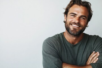Smiling man with beard and wavy hair wearing a casual green long-sleeve shirt against a plain light background with arms crossed