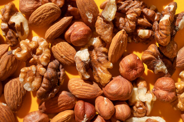 Close-up of scattered different nuts: walnut, almond, hazelnut top view on yellow background. Assorted peeled nuts, organic healthy snack. Food background