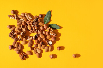 Different nuts, walnut, hazelnut, almond and green leaves on yellow background flat lay top view. Mix of tasty healthy nuts, snack, appetizer. Food background. Sunlight with long shadows