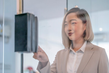 portrait through glass door,young asian female company employee using biometric fingerprint system...