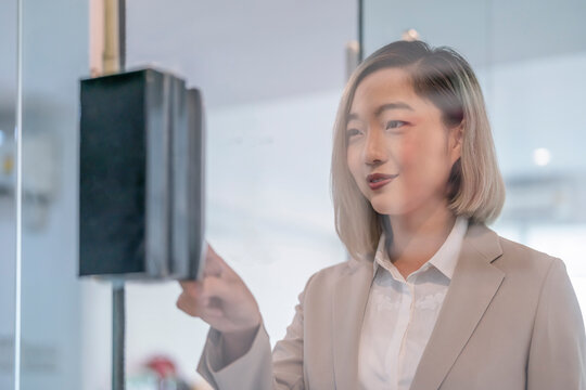 portrait through glass door,young asian female company employee using biometric fingerprint system for time attendance and door access