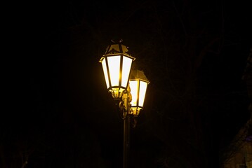 Vintage street lamps illuminate a dark urban setting, casting a warm glow against the night sky, creating a nostalgic atmosphere and enhancing the charm of the surroundings
