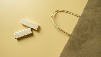 Paper shopping bag with wooden blocks on yellow background, concept of retail, eco packaging, e-commerce, online shopping, sustainability, and consumer lifestyle.