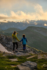Woman and her son are standing on some rocks and watching the brilliant sunset.
