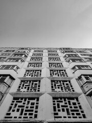Monochrome low-angle view of a tall building with a unique, perforated concrete facade featuring a repeating geometric pattern against a clear sky
