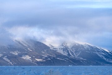 Fog drifts over snow covered mountains of Svalbard, a striking Arctic scene blending raw wilderness...