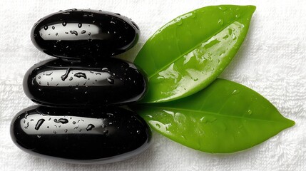 Three smooth, black stones rest atop each other, juxtaposed with vibrant green leaves, evoking a sense of tranquility and natural beauty.