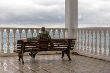 A man on a bench on the embankment looks into the distance. Inclement weather at sea. Thunderclouds and a storm at sea. Relaxing by the sea. A bench for relaxing with a view of the sea.