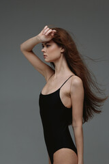 Fototapeta premium Profile of a young woman in a black bodysuit shielding her eyes with her hand, showing natural pose and neutral expression.