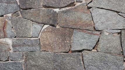 A close-up of a wall constructed from natural stones of varying shapes and sizes, highlighting its rough and uneven texture.