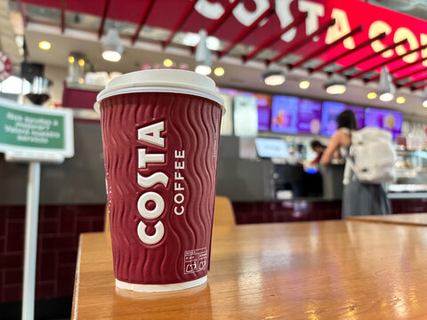 Alicante, Spain - August 26, 2025: Costa Coffee cup on wooden table in cafe, with vibrant background showcasing coffee shop ambiance and customer interaction, inviting coffee lovers to enjoy it
