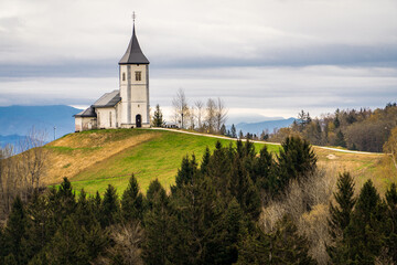 Hermosa postal de la Iglesia de Jamnik, en Eslovenia, ubicada en la cima de una colina rodeada de bosques, un día de otoño	