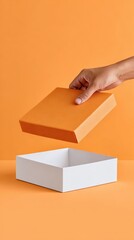 Hand holding an orange box above an empty white box on a vibrant orange background, showcasing the concept of packaging and gift presentation in a minimalist style