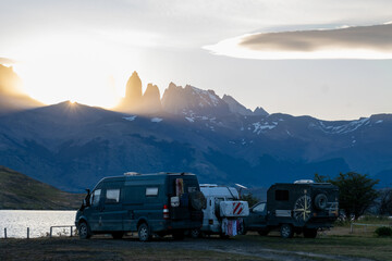 A group of friends in camper vans camp by a Patagonian lake, with the stunning Torres del Paine mountains at sunset. A celebration of adventure and community