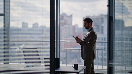 Elegant business owner messaging smartphone panoramic window. Frustrated manager