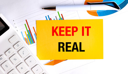 Keep it real phrase on yellow card with colorful charts, pen and calculator on white office...