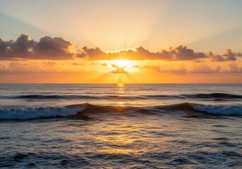 Obraz premium Golden hour ocean sunset with gentle waves and cloudy sky