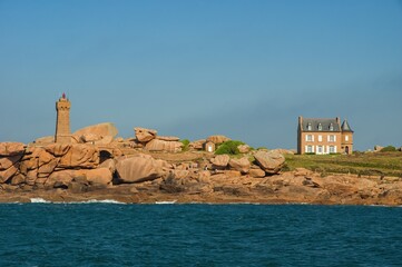 Picturesque view of the famous Ploumanac'h lighthouse (Mean Ruz) on the Pink Granite Coast in Brittany, France. The rugged shoreline with unique rose-colored granite rocks, a traditional French house,