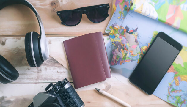 Travel essentials flat lay with passport, map, camera, sunglasses, headphone, and phone for vacation, tourism, and adventure trip