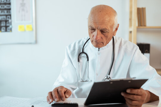 Elderly senior male Accounting doctor in white coat with stethoscope calculating bookkeeping finance and hospital budget