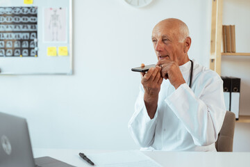 Senior elderly male doctor recording audio message to a patient using smartphone mic. copy space