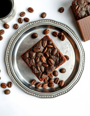 top view of delicious brownie piece with coffee beans and chocolate on silver tray on white background, panoramic shot, hyperrealism. isolated with white highlights