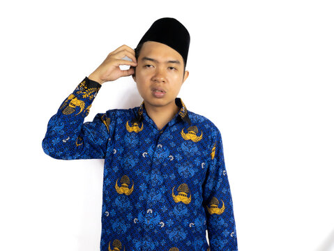 An Indonesian Male civil servant wearing a blue Batik Korpri uniform poses makes a thinking gesture, expressing confusion or concentration, standing in front of a white backgound. PNS Concept.