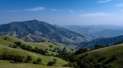 Obraz premium Lush green hills and distant mountain ranges under a clear blue sky.