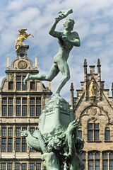 Fototapeta premium Brabo Fountain in Antwerp, Belgium, bronze statue of Silvius Brabo throwing a severed hand. Behind the fountain are ornate Flemish buildings with gabled roofs and decorative facades,