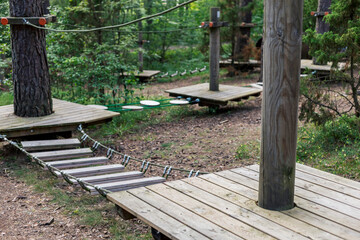 Wooden platforms and rope bridges create an engaging climbing experience in a tree climbing park surrounded by vibrant greenery. The area offers a unique outdoor accessibility for young adventurers