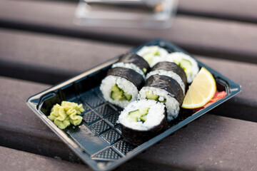 Sushi rolls filled with cucumber are neatly arranged on a black tray. A dollop of wasabi and a slice of lemon complement the rolls, creating an appealing presentation