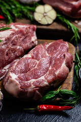 Raw pork cuts on a wooden board with herbs and tomatoes, ready to be cooked