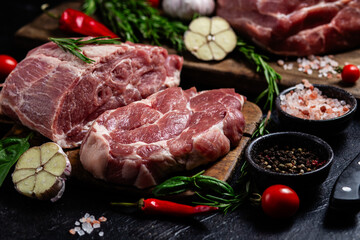 Raw pork cuts on a wooden board with herbs and tomatoes, ready to be cooked