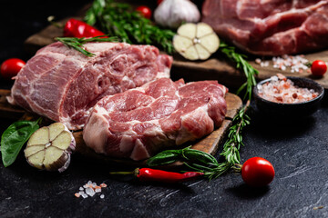 Raw pork cuts on a wooden board with herbs and tomatoes, ready to be cooked