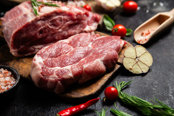 Raw pork cuts on a wooden board with herbs and tomatoes, ready to be cooked