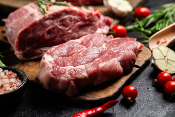 Raw pork cuts on a wooden board with herbs and tomatoes, ready to be cooked