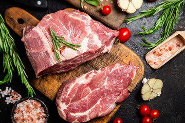 Raw pork cuts on a wooden board with herbs and tomatoes, ready to be cooked