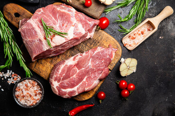 Raw pork cuts on a wooden board with herbs and tomatoes, ready to be cooked