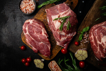 Raw pork cuts on a wooden board with herbs and tomatoes, ready to be cooked