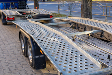 Obraz premium A heavy-duty car hauler sits parked on a city street, displaying its metal ramps and wheels under the afternoon sunlight