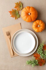 Autumn-themed table setting featuring white plates, wooden fork, vibrant orange pumpkins, and colorful leaves, creating a warm and inviting seasonal atmosphere for dining
