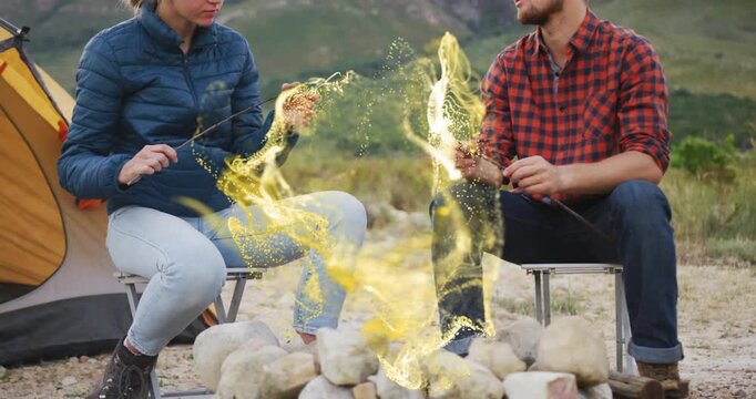 Arriving at campsite couple placing chairs and roasting sausages over gold swirl for camping meal