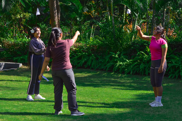 Three girls stand side by side in a lush tropical park, smiling as they throw paper airplanes joyfully into the bright morning air.