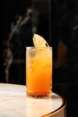 Refreshing cocktail with orange slice and ice cubes in a tall wine glass, served on a marble table. Sparkling drink with bubbles, elegant presentation in a dark background